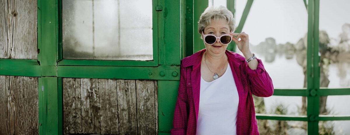 Susanne, wie sie mit einer Sonnenbrille auf, lachend in die Kamera blickt