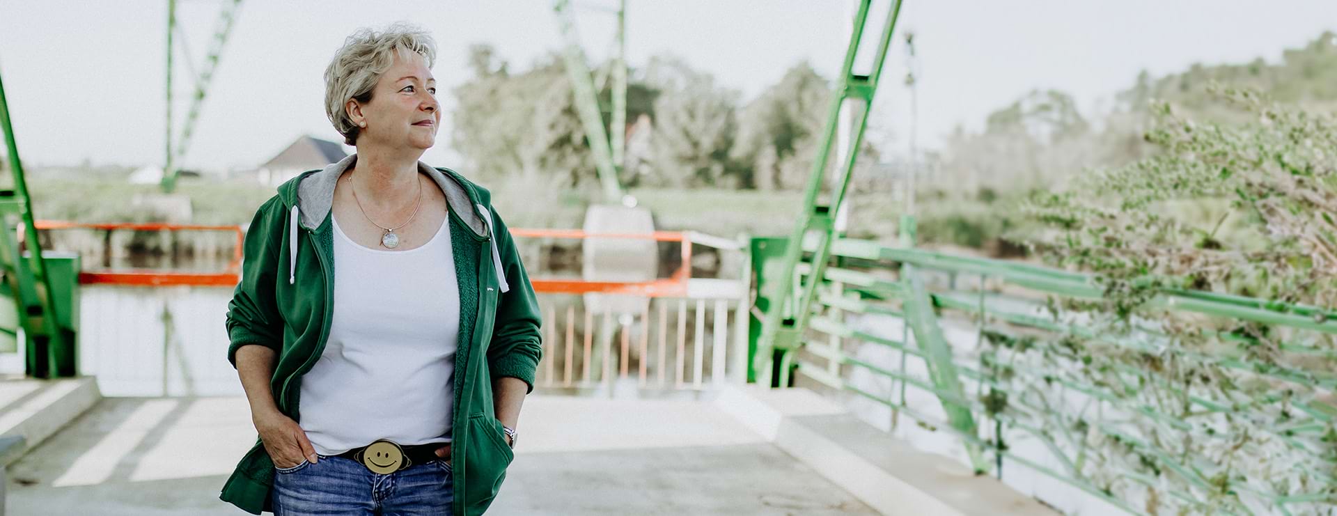 Susanne schlendert lächelnd auf einer Brücke